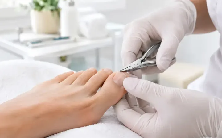 Pėdų priežiūros specialistė žnyplėmis kerpa kojos nagą